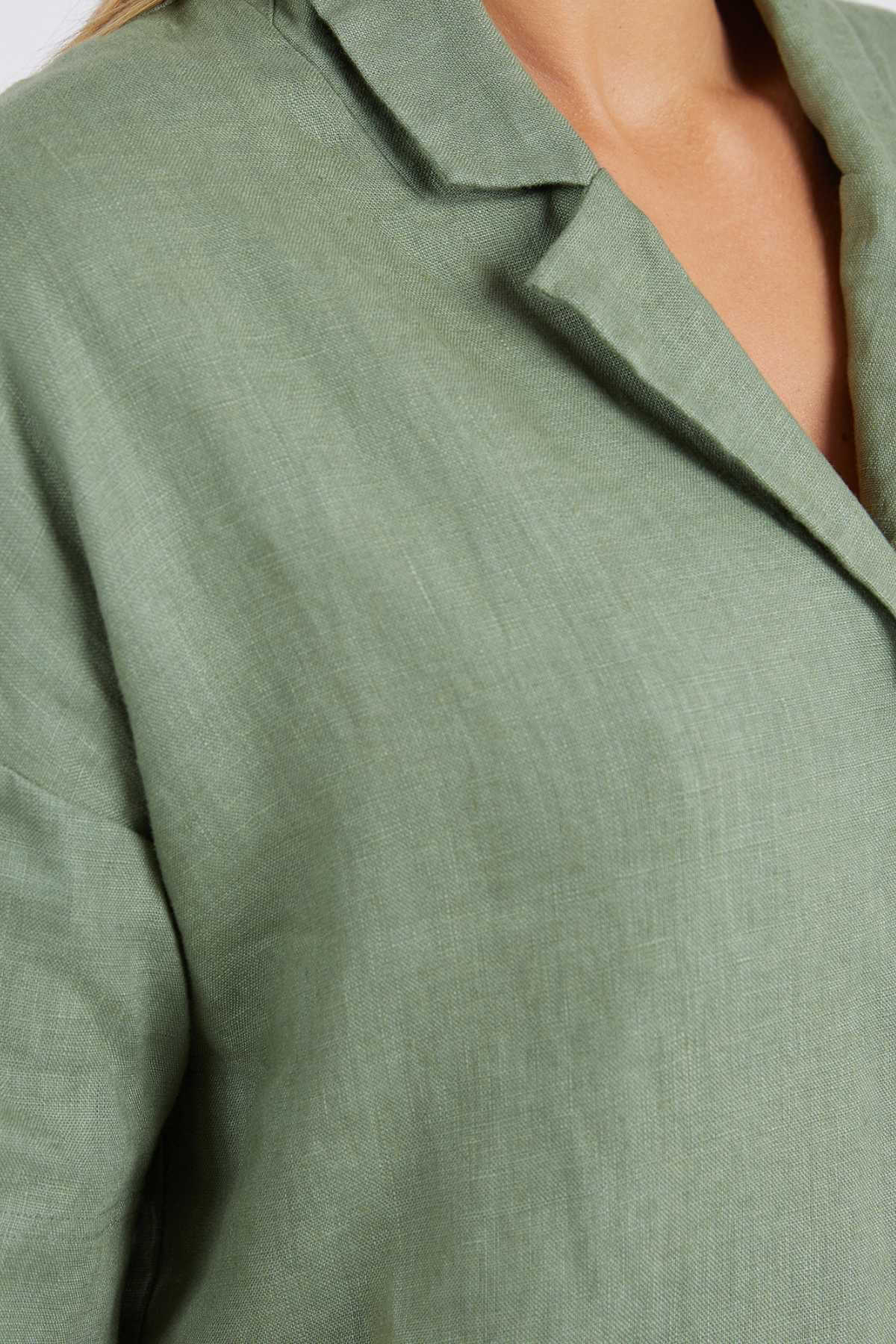 A detailed shot shows the shoulder and chest area of a relaxed-fit Foxwood Aubrey Shirt in light olive green linen, highlighting its button-through placket and fabric texture.