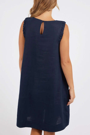 A woman wears the Foxwood Bastia Dress, a navy blue sleeveless, knee-length A-line dress with ruffled shoulder details, shown from the back against a plain background.