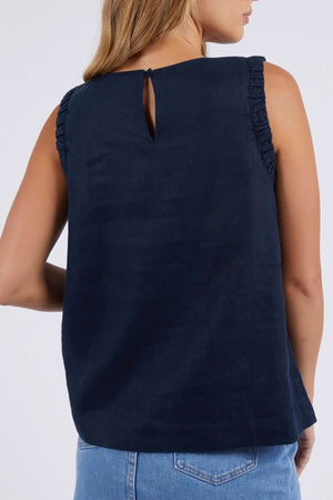 A woman is seen from behind wearing the Foxwood Bastia Top—a relaxed-fit, navy sleeveless top with ruffled armholes and a keyhole neckline—paired with light blue jeans.