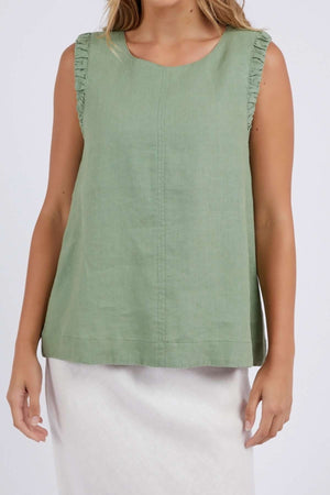 Wearing a trendy Foxwood Bastia sleeveless light green top with ruffled edges, stylishly paired with a white skirt, set against a simple light gray background.
