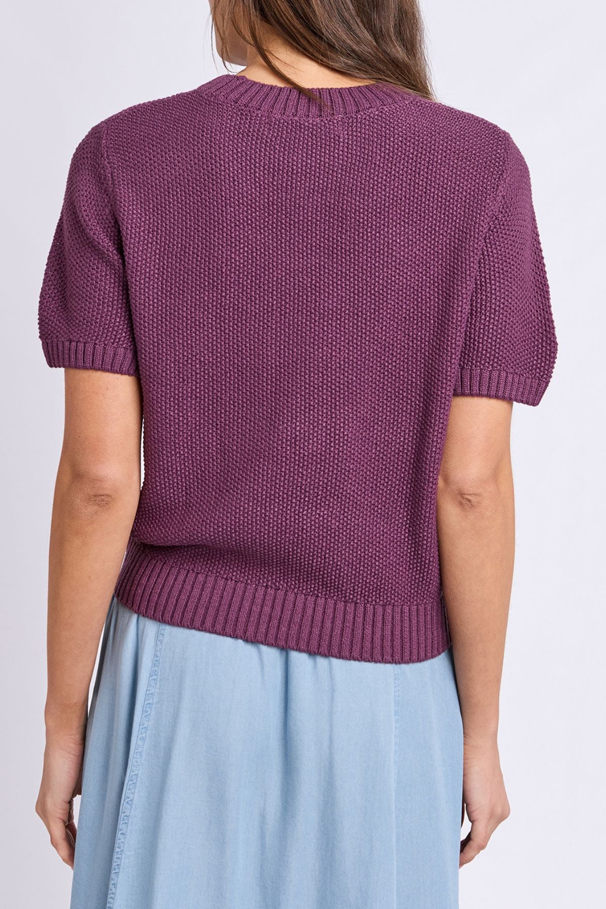 A person is shown from the back against a plain background, wearing the Foxwood Blair Short Sleeve Knit—a textured purple sweater—paired with a light blue skirt.