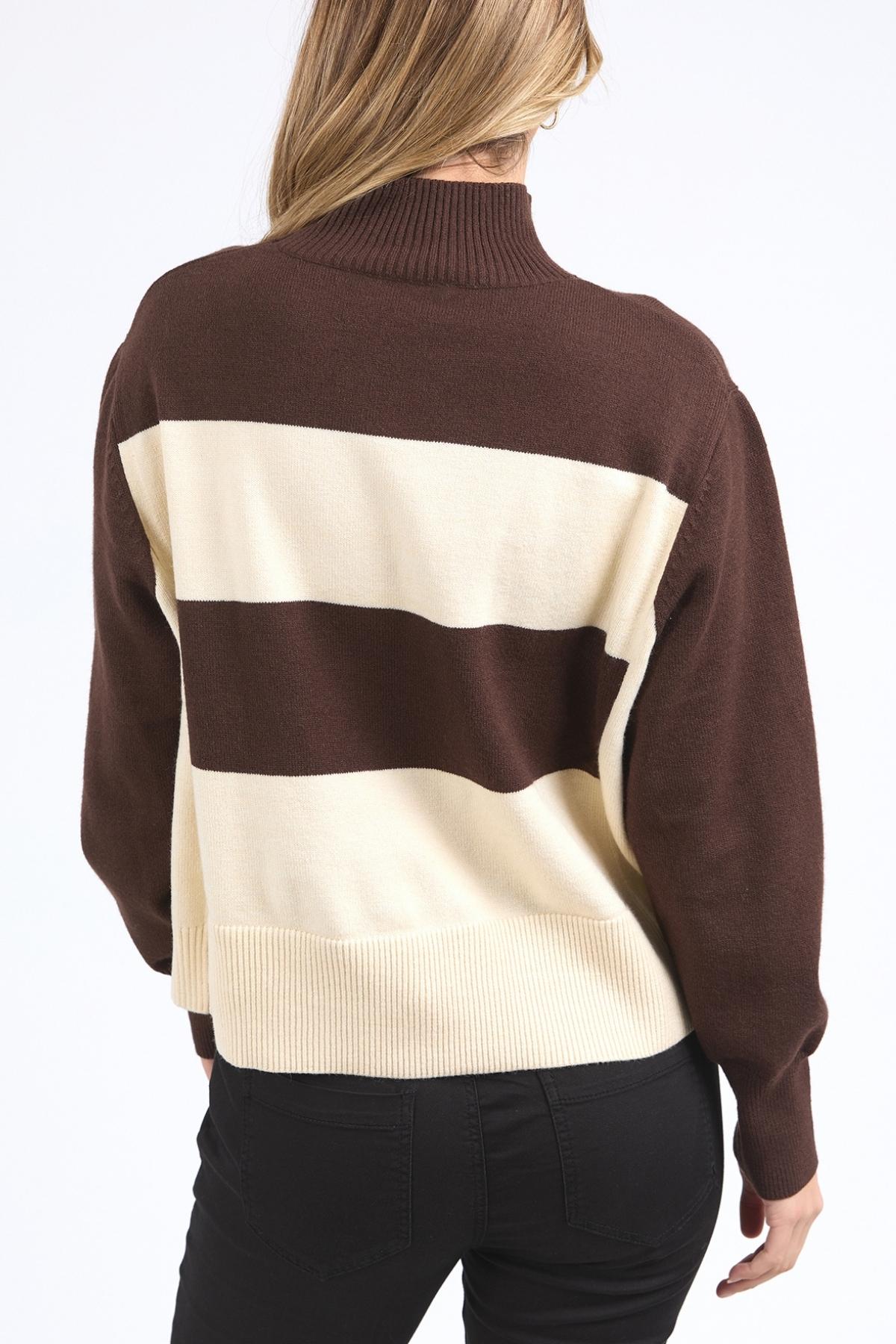 A person with long blonde hair wears the Foxwood Canterbury Knit, a wool-cashmere blend sweater with wide brown and cream stripes, paired with black pants and facing away from the camera against a white background.