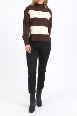 A person wearing the Foxwood Canterbury Knit, featuring brown and cream yarn-dyed stripes, with black pants and black ankle boots stands against a plain white background. The person’s face is not visible.