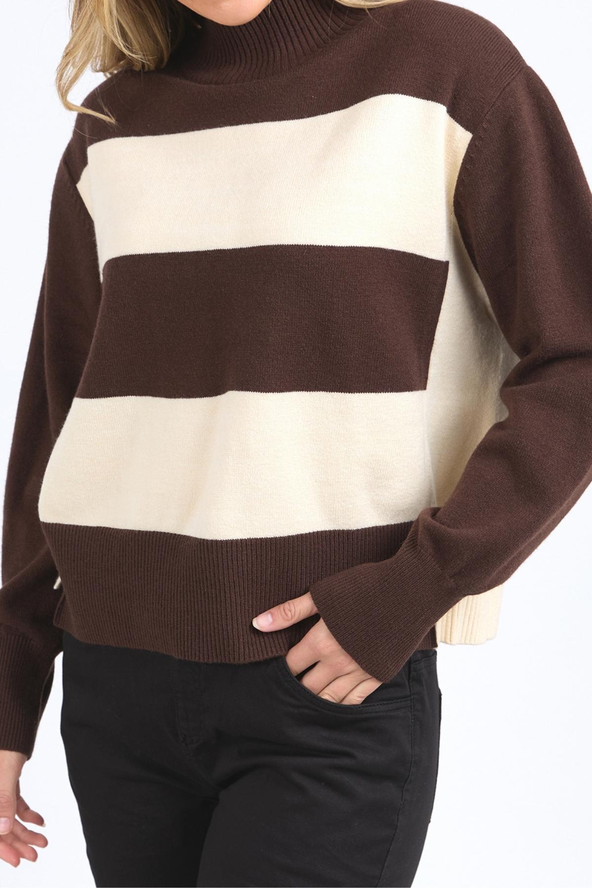 A person wears the Foxwood Canterbury Knit—a brown and cream yarn-dyed striped sweater—with black pants, standing with one hand in a pocket against a plain background.