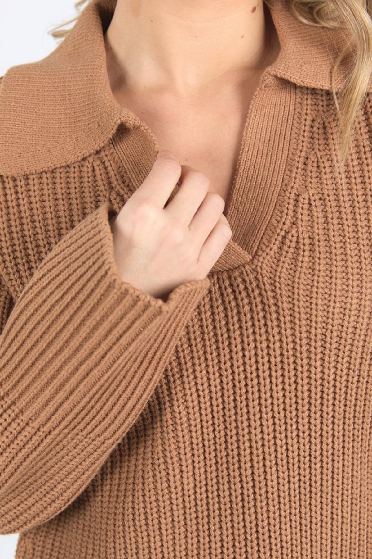 Close-up of a person wearing the Foxwood Carlton Knit, a relaxed fit light brown sweater with a wide collar. They're holding the collar with one hand, hair visible on the right, highlighting its comfort and stylish design.
