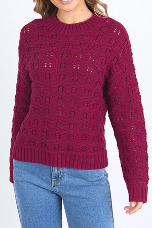 A woman wears the Foxwood Carter Knit, a textured dark pink sweater with a round neck and long sleeves, styled with light blue jeans against a white background.