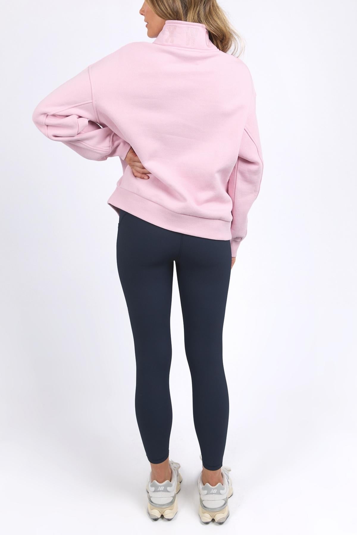 A person faces away from the camera, wearing a soft cotton Foxwood College Zip Crew with an embroidered collar, paired with dark blue leggings and white sneakers, set against a plain white background.