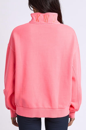 A person with long dark hair faces away from the camera, wearing the Foxwood College Zip Crew in bright pink cotton with a loose fit, high embroidered collar, and subtle lettering, set against a plain background.