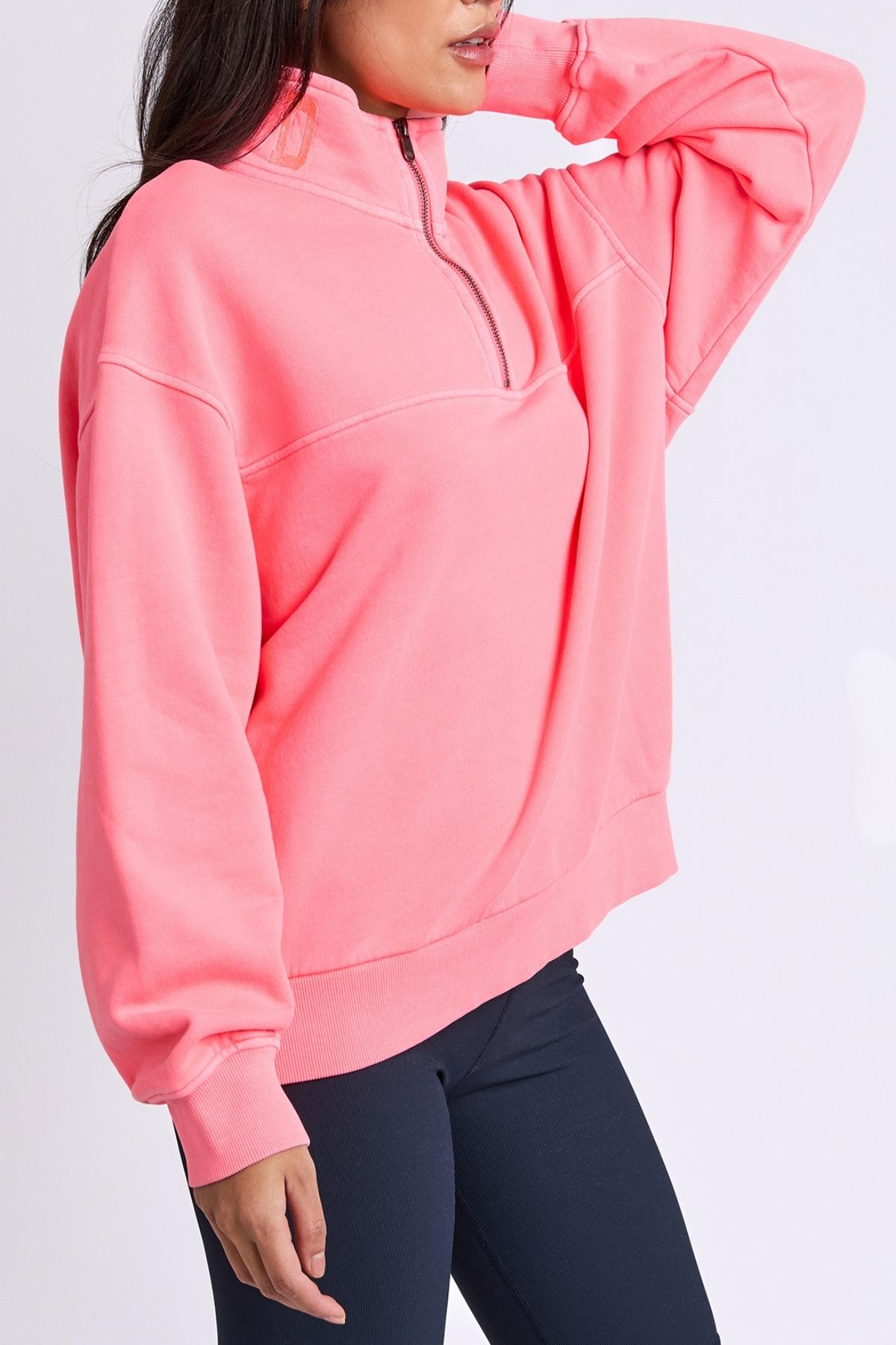 Wearing the loose, bright pink Foxwood College Zip Crew with an embroidered collar and long sleeves, paired with dark leggings, a person poses hand behind head against a plain background.