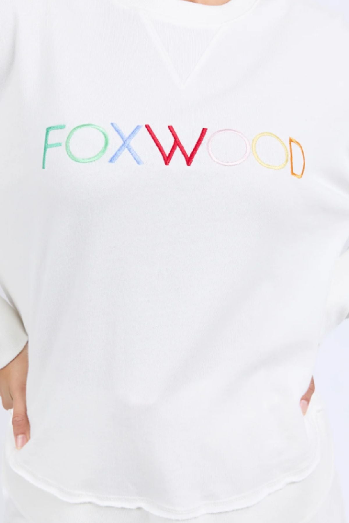 A person wearing the Foxwood Simplified Confetti Crew, a white cotton sweatshirt featuring multicoloured "FOXWOOD" embroidery on the front.