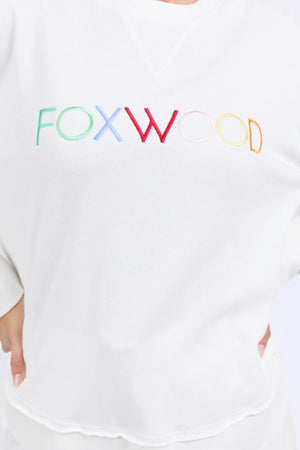 A person wearing the Foxwood Simplified Confetti Crew, a white cotton sweatshirt featuring multicoloured "FOXWOOD" embroidery on the front.