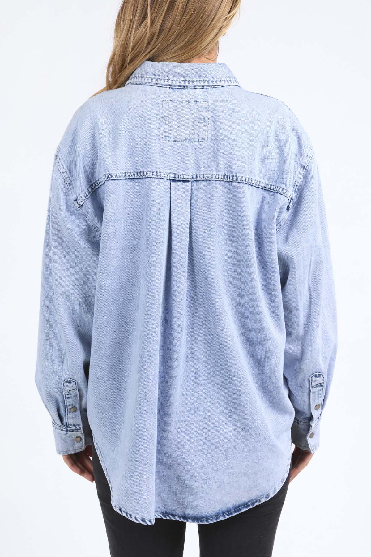 A person with long, light brown hair wears the Foxwood Daisy Over Shirt in relaxed fit and light blue 100% cotton, shown from the back against a white background.