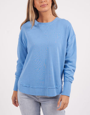 A person wearing a Foxwood Delilah Crew in plain blue and light gray jeans stands against a white background.