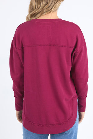 A person with long, light brown hair is seen from the back wearing a loose-fitting Foxwood Delilah Crew in dark pink and blue jeans against a plain white background.