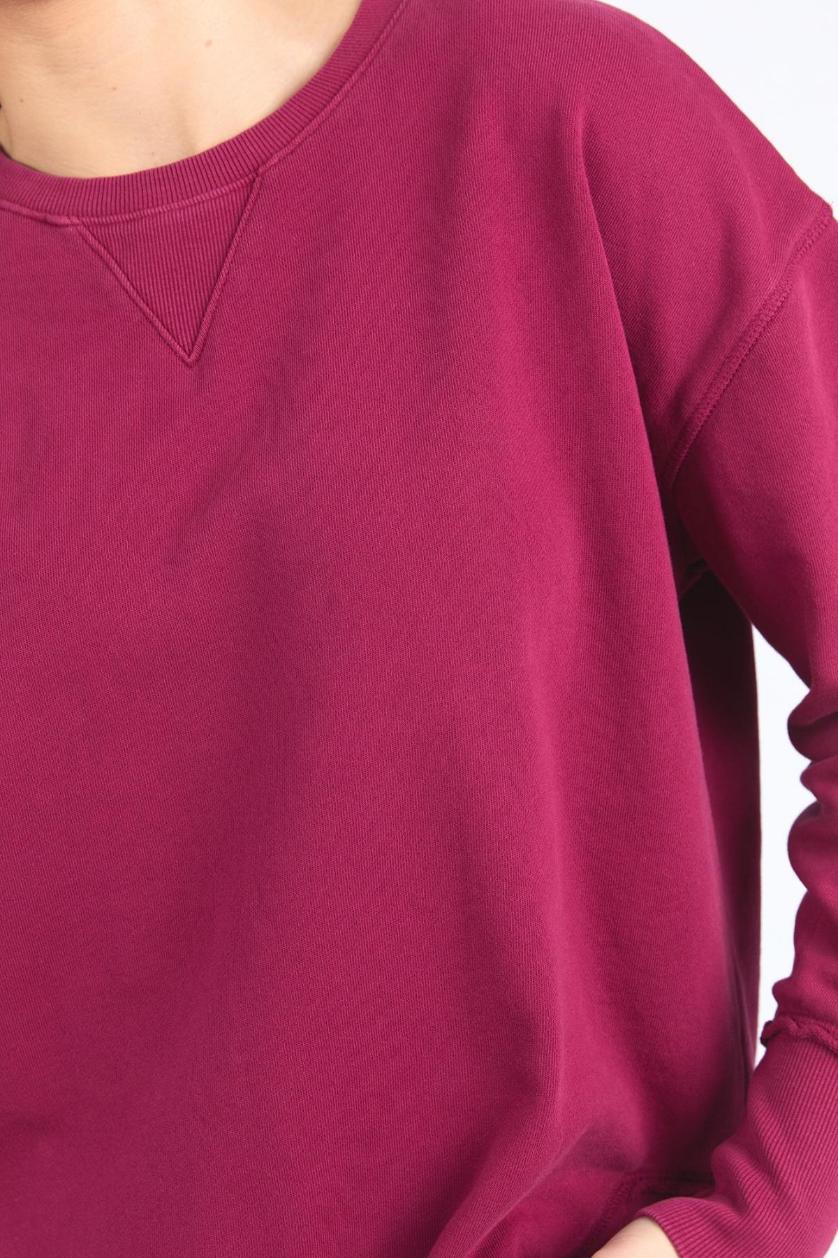 Model wears the Foxwood Delilah Crew, a long-sleeved, raspberry cotton jumper featuring a ribbed crew neckline and V-shaped stitch detail, shown from the shoulders to mid-torso.
