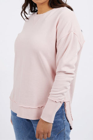 A person wearing the Foxwood Delilah Crew in light pink with raw hem details and blue jeans, standing against a plain white background.