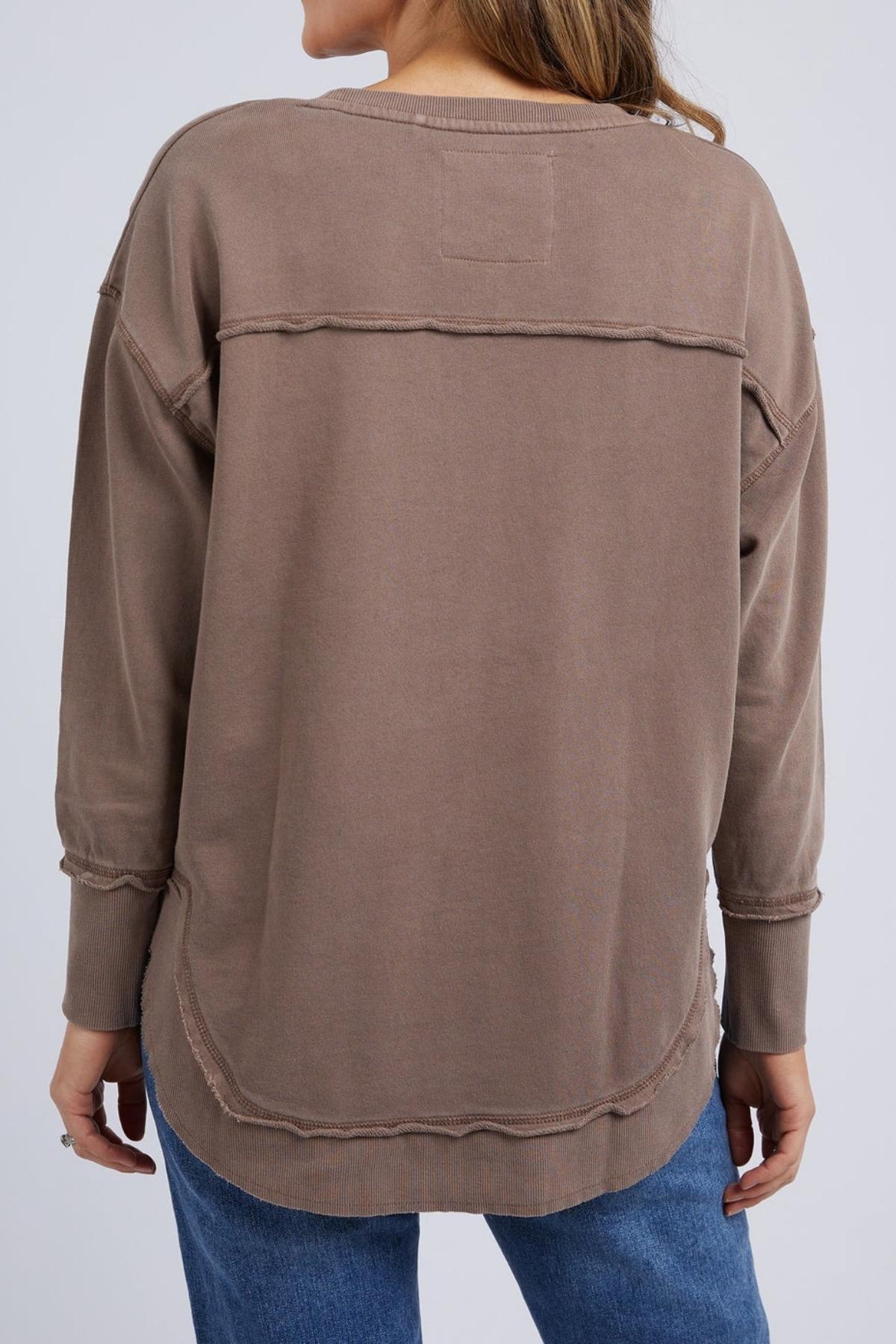 A person is seen from the back wearing a loose-fitting Foxwood Delilah Crew in taupe with exposed seams and blue jeans.