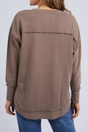 A person is seen from the back wearing a loose-fitting Foxwood Delilah Crew in taupe with exposed seams and blue jeans.