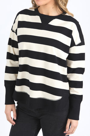 A person models the Foxwood Delilah Stripe Crew—black and white horizontal stripes, long sleeves, black pants—against a plain white background. The head is partially out of frame. Made from 100% cotton for comfort.