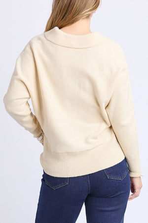 A person with long, light brown hair is shown from the back, wearing the Foxwood Elea Knit Polo in cream and dark blue jeans against a plain light background.