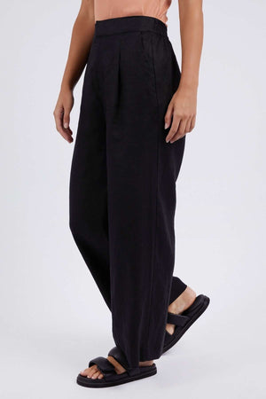A person in black Foxwood Elina Wide Leg Pants and black slide sandals, with a peach-hued top showing at the waist, stands against a white background.