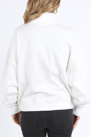A woman with wavy, light brown hair is shown from behind, wearing the Foxwood Ember Zip Thru jacket and black jeans against a plain white background.