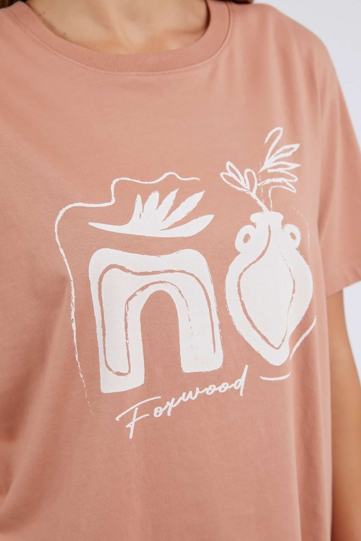 The Foxwood Etched Geo Tee offers a relaxed fit and is crafted from 100% cotton. This salmon t-shirt showcases abstract white designs with geometric shapes and a vase with leaves, complemented by the stylish "Foxwood" print beneath the motifs.