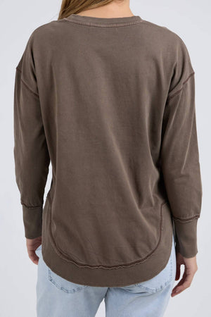 A person is shown from the back against a plain light background, wearing the relaxed fit Foxwood Farrah Long Sleeve in brown and light blue jeans.