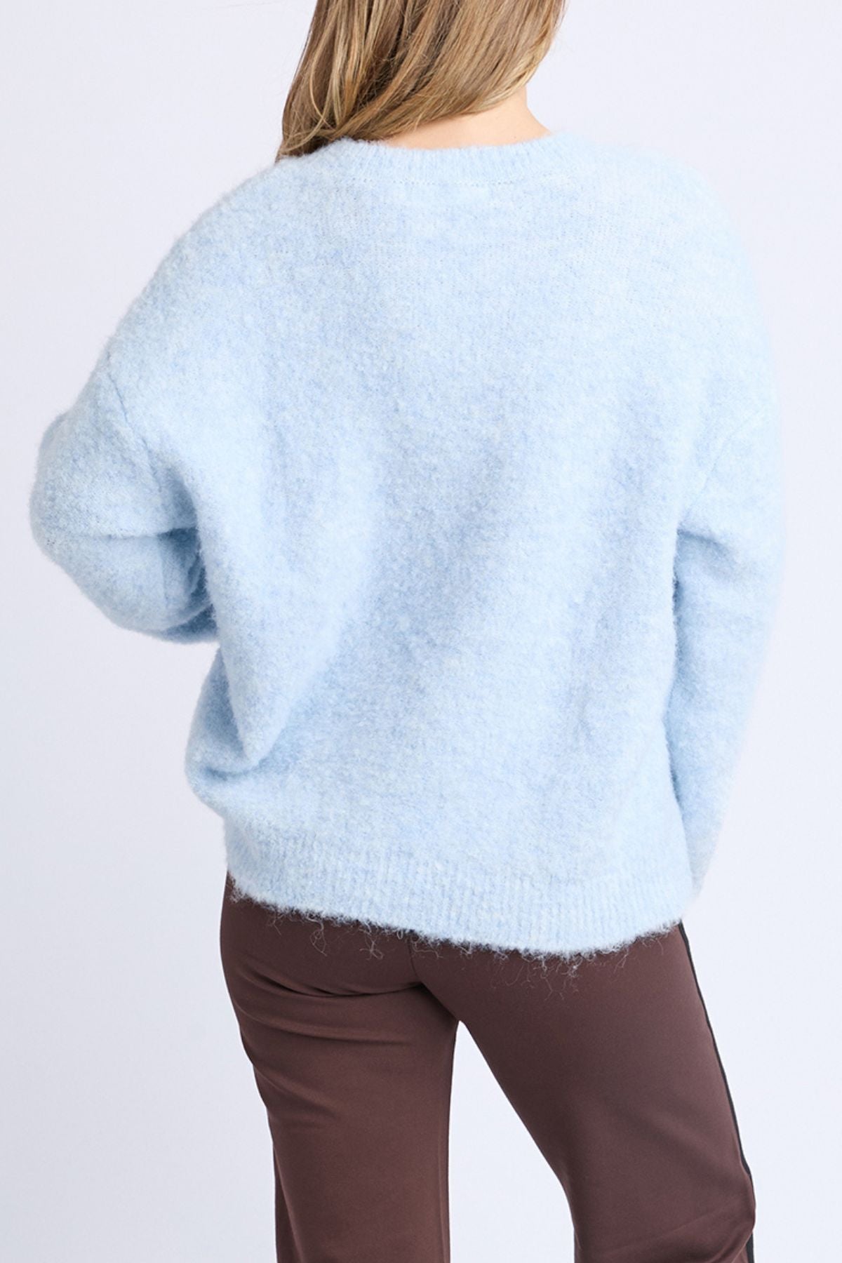 A person with light brown hair is wearing the Foxwood Flint Knit Crew sweater and brown pants, facing away from the camera against a plain light background.