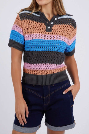 Wearing the Foxwood Gazelle Stripe Knit short-sleeve polo with peach, gray, blue, and pink horizontal stripes, the person pairs it with dark rolled denim shorts and casually rests a hand in one pocket.