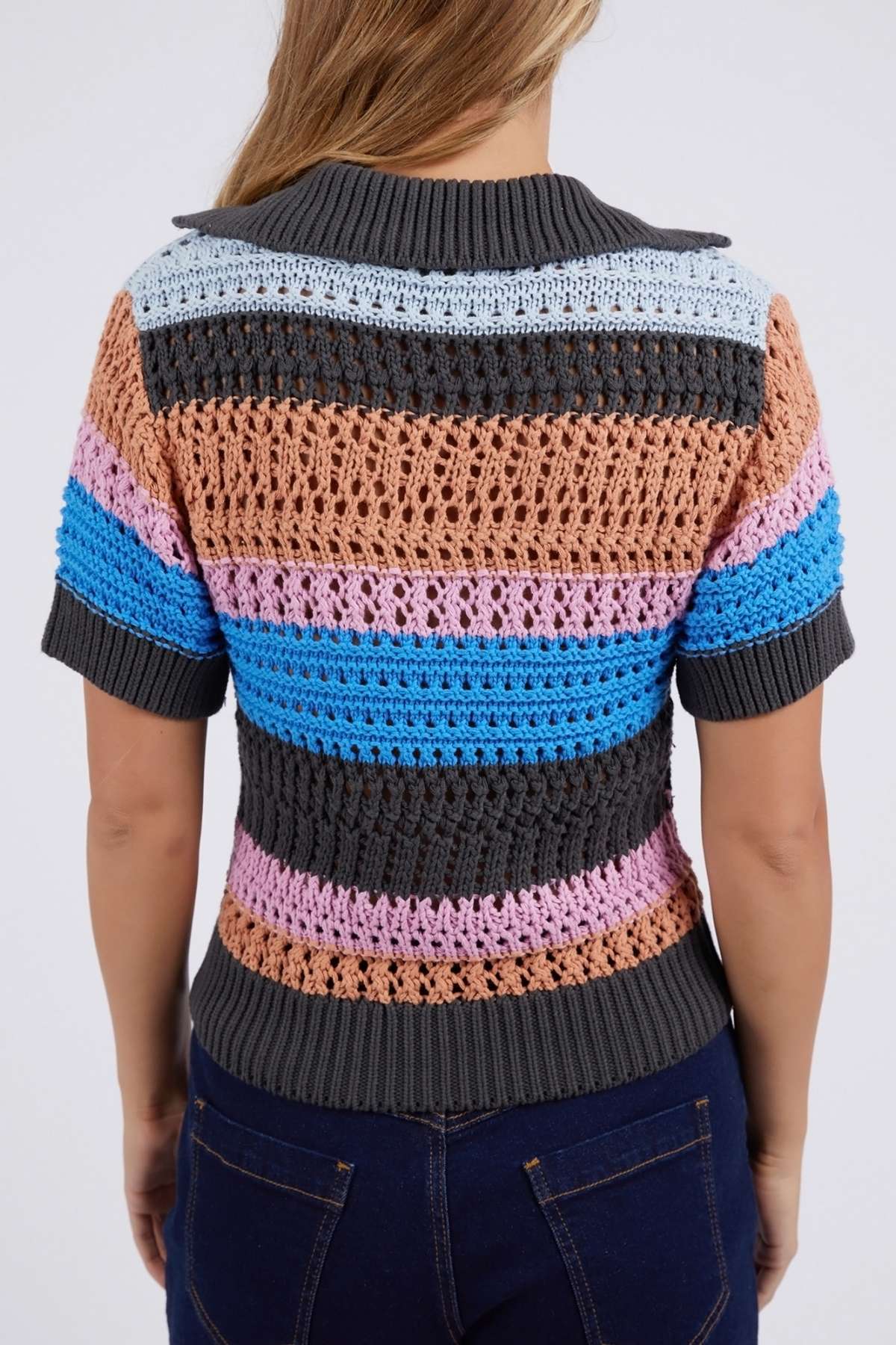 A person in a short-sleeve Foxwood Gazelle Stripe Knit sweater with gray, brown, pink, blue, and light blue stripes stands facing away wearing dark jeans. This cotton top features a textured pattern and versatile colors.