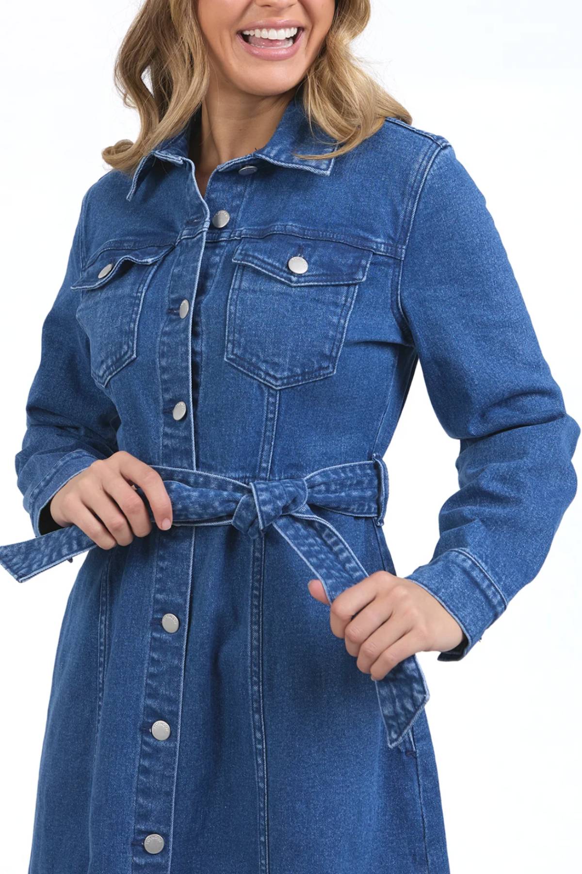 A woman smiles wearing the Foxwood Genevieve Denim Dress, a midi-length, button-down denim style featuring a belted waist and chest pockets for both fashion and function.