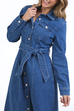 Woman wears the Foxwood Genevieve Denim Dress, a stylish long-sleeved midi with front button closure, chest pocket, and waist tie—posing against a plain white background to highlight its fashion and function.