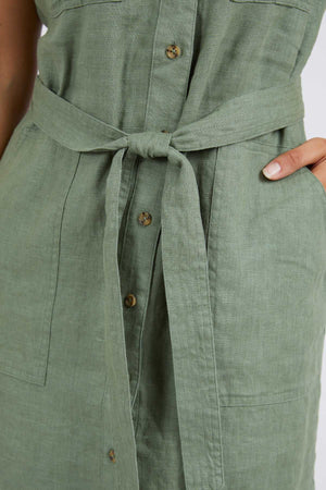 Close-up of a person wearing the Foxwood Harlow Dress; this smart-casual piece features green linen, brown buttons, a belted waist, and side pockets—perfect for a polished summer look.