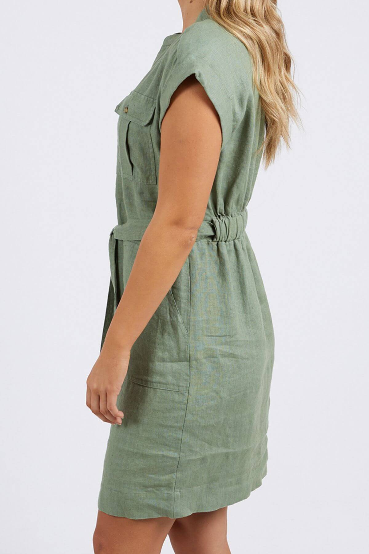 A woman models the Foxwood Harlow Dress in light green linen, styled smart-casual, shown in a side view against a plain white background.