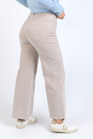 Wearing Foxwood Henrietta Cord Pants and white Veja sneakers, a person stands with their back to the camera, hands on hips, against a plain light background.