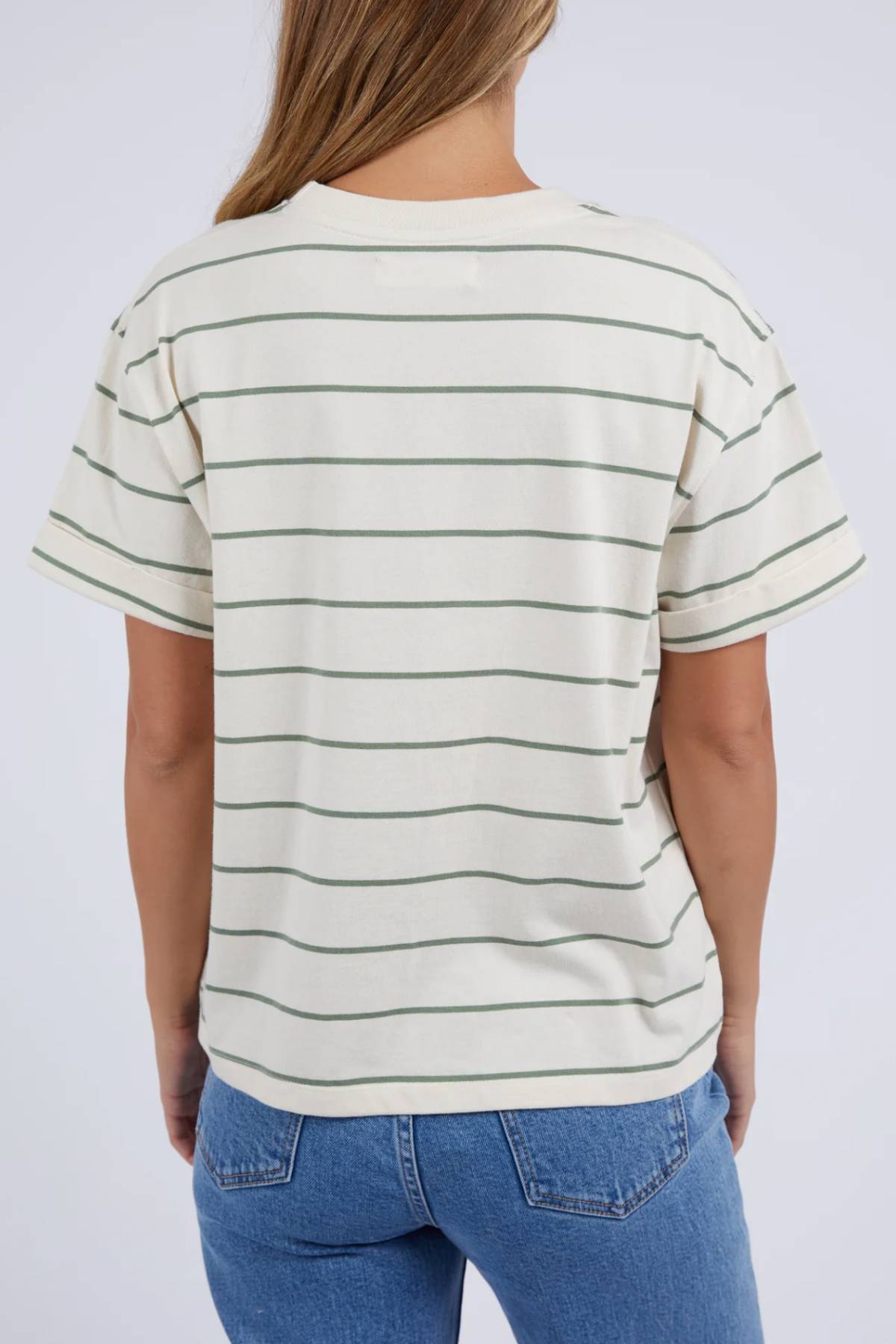 A person, seen from behind, is wearing the Foxwood Huntleigh Stripe Tee—a cream-colored t-shirt adorned with thin green stripes—stylishly teamed with blue jeans. Crafted from 100% cotton, it pops against the plain light gray background.