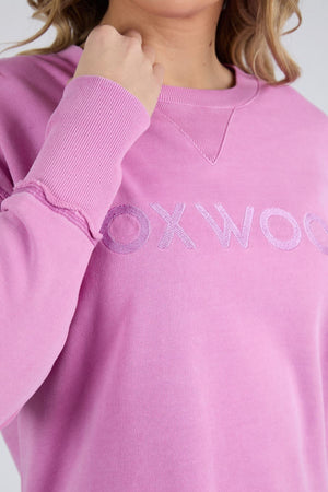 Someone wearing the Foxwood Illusion Crew, a light purple relaxed-fit sweatshirt made from soft cotton fleece, featuring a partially visible embroidered "OXWOO" on the front and shown from shoulders to mid-torso.