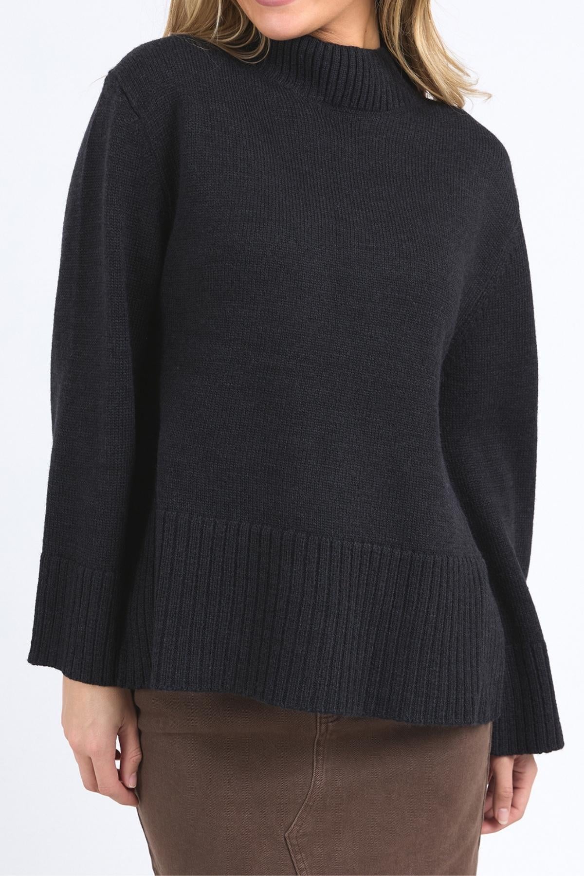 A person wears a Foxwood Jude Knit sweater with a mock neck, long sleeves, and wide hem, styled with a brown skirt. The face is not visible.