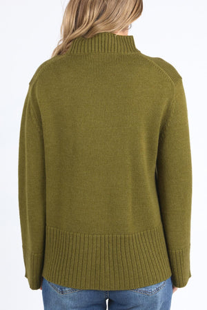 A person with long, light brown hair is seen from behind wearing the Foxwood Jude Knit, a green sweater featuring a relaxed fit with ribbed hem, cuffs, and mock neck collar, styled with blue jeans against a plain white background.