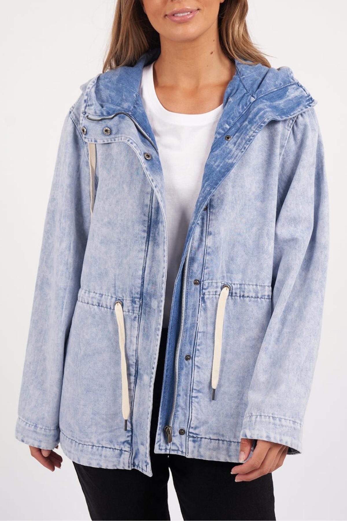 A person wearing the Foxwood Kingston Anorak—a light blue, vintage-washed denim jacket with a hood, adjustable waist cord, and white drawstrings—over a white t-shirt, shown from shoulders to hips.