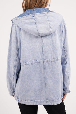 A person is seen from the back wearing a light blue Foxwood Kingston Anorak in vintage washed rigid denim, featuring visible stitching, a loose fit, an adjustable waist cord, and a hood worn down with hands at their sides.