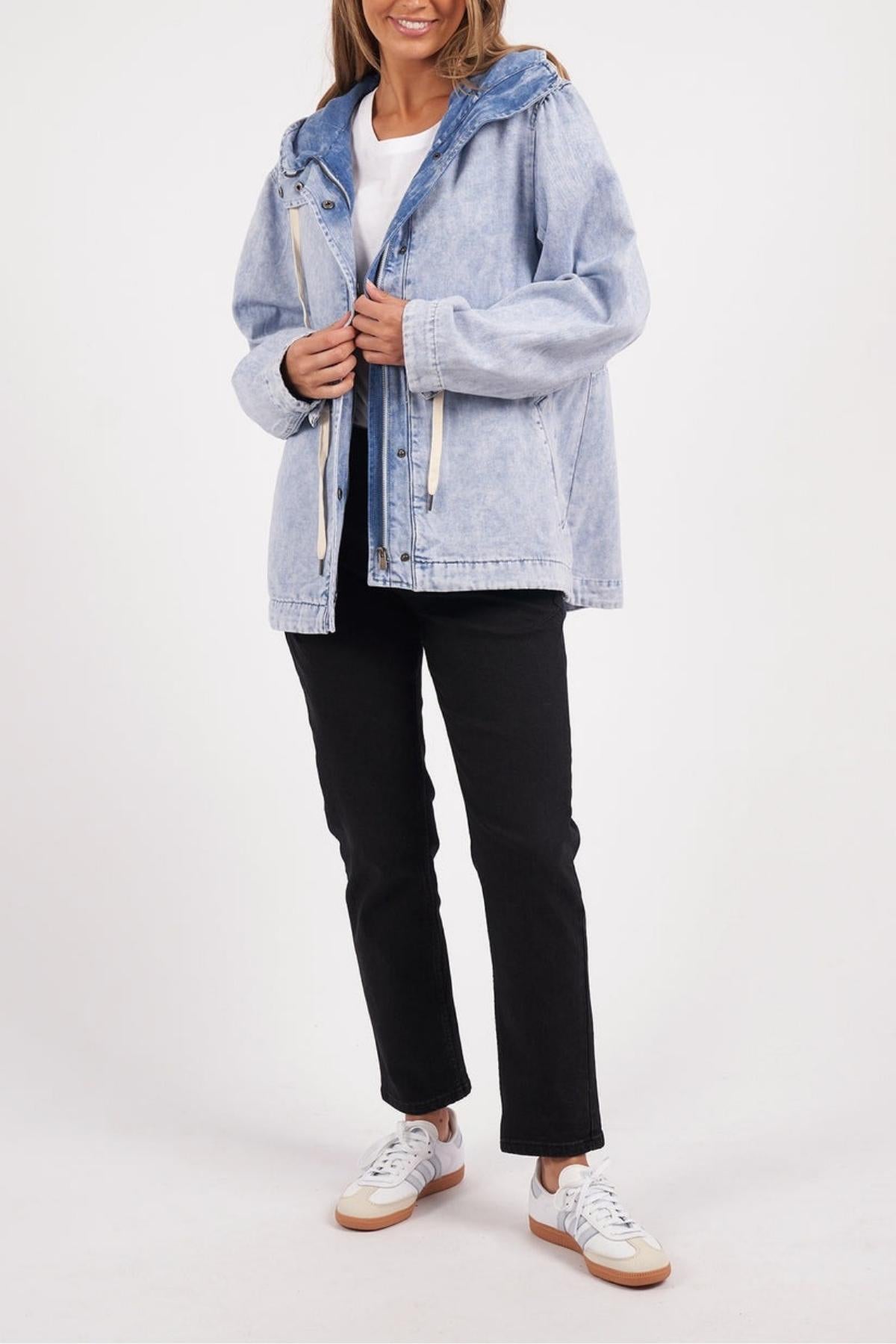 A woman wears the Foxwood Kingston Anorak with an adjustable waist cord over a white top, black pants, and white sneakers, standing against a plain white background holding the jacket near the zipper.