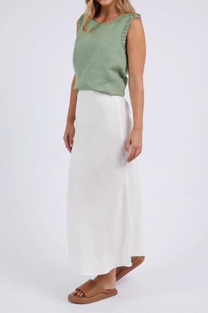 A person models a sleeveless, light green top paired with the Foxwood Lyon Slip Skirt—a long, white linen blend skirt featuring an elastic waist. They complete the look with tan sandals against a plain backdrop.