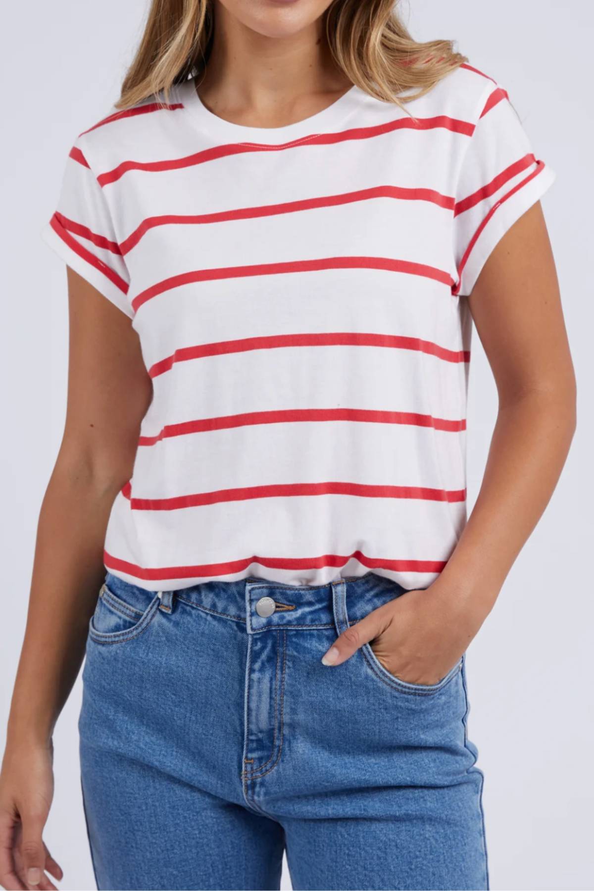Wearing a Foxwood Manly Stripe Tee with red stripes on white Pima cotton jersey, paired with classic blue jeans, they casually slip a hand into their pocket, exuding effortless style.