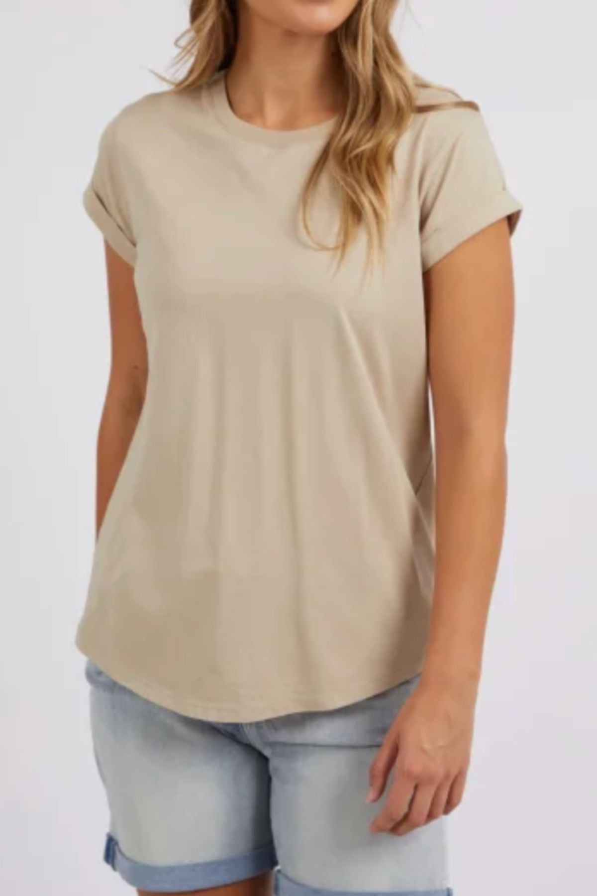 A woman wears the Foxwood Manly Tee, made from soft 100% cotton with rolled cuffs, paired with light denim shorts. Against a plain backdrop, her partially out-of-frame face adds to the effortless, casual chic style.