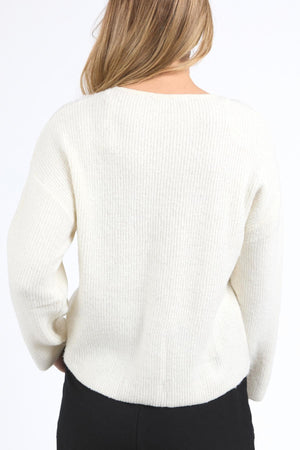 A person with light brown hair is seen from the back, wearing a cozy and stylish cream Foxwood Murphy Knit Cardi with a relaxed fit and black pants against a plain white background.