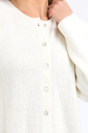 A person wears the Foxwood Murphy Knit Cardi—a textured, white, long-sleeved cardi with a relaxed fit—shown from shoulders to waist, with one hand touching their neck.