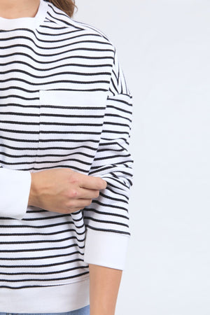 A person adjusts the cuffed sleeve of their left arm while wearing the Foxwood Original Stripe Crew, a relaxed fit jumper with black horizontal stripes, shown partially against a plain light background.
