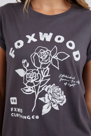 Wearing the Foxwood Rosette Tee—a dark gray, 100% cotton shirt with white rose and leaf illustrations, "FOXWOOD" above the design, and "FXWD CLOTHING CO" in small text below—adds stylish floral flair.